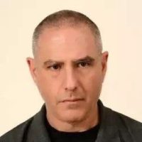 איש בעל מראה רציני עם שיער אפור קצר וחולצה כהה.